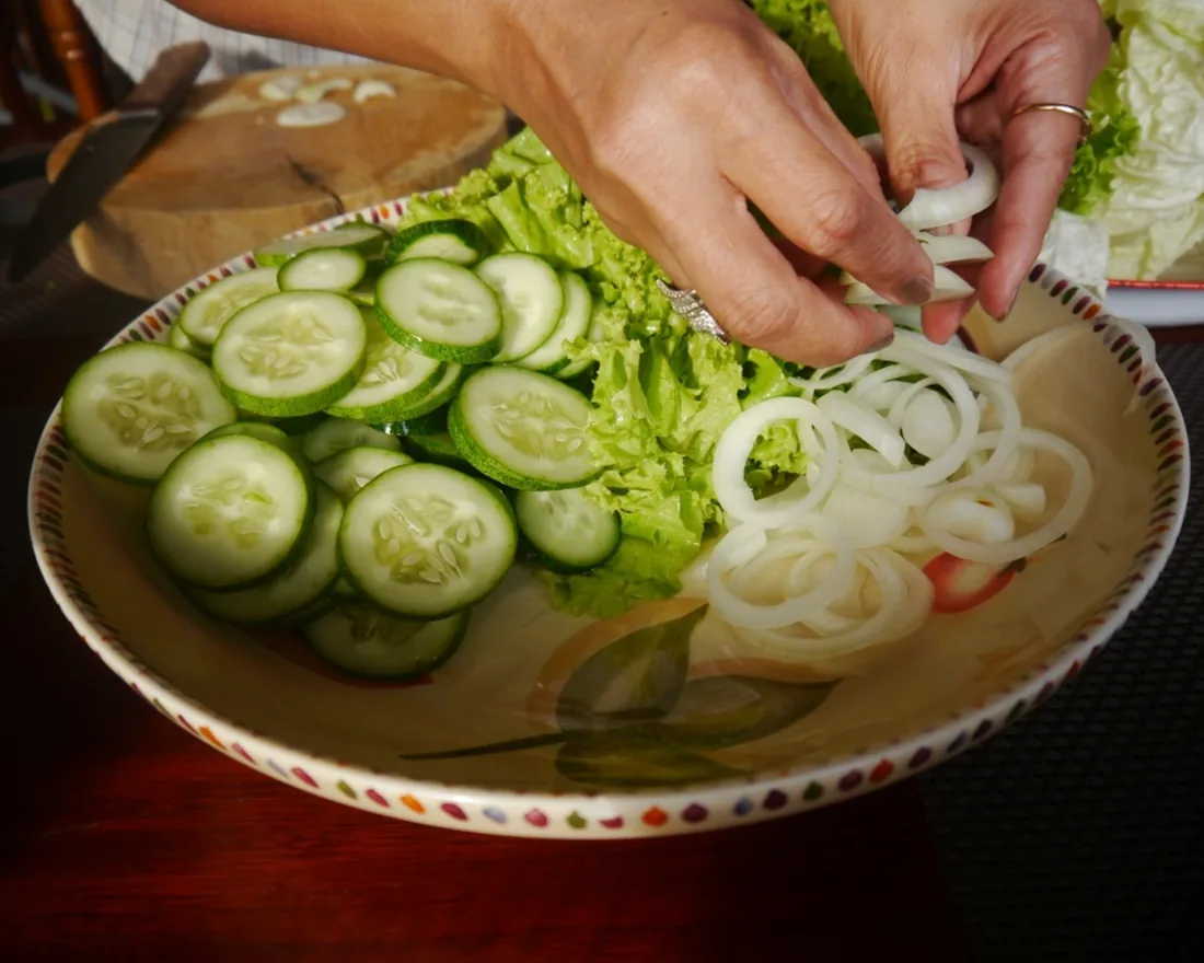 Tangan menata irisan mentimun dan bawang di atas piring saat kelas memasak